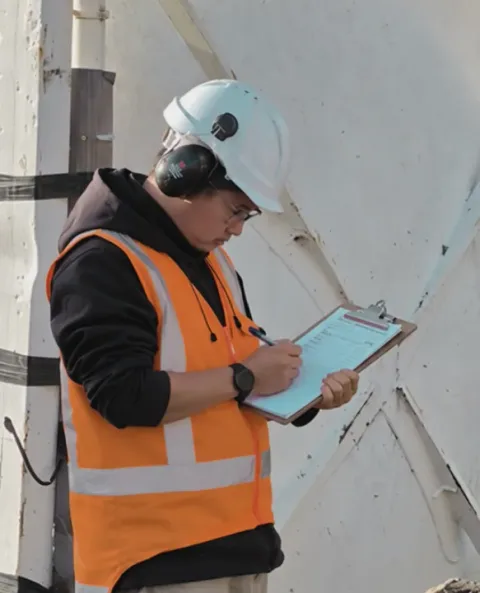 Site worker in a hard hat and high-visibility vest recording an inspection beside a concrete structure.