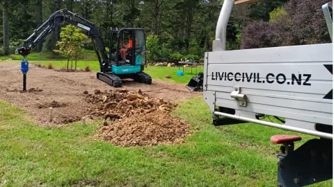 Livic mini excavator drilling with an auger at a landscaped site.